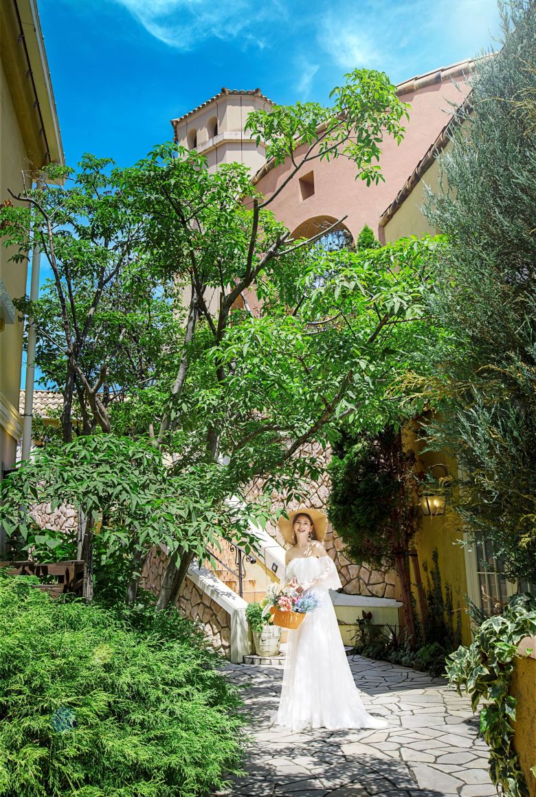 さいたま市の結婚式場アネーリ大宮。南欧風の螺旋階段と黄色い壁が続く街並みで、麦わら帽子の花嫁が佇む。まるで海外リゾートのようなナチュラルな一枚。