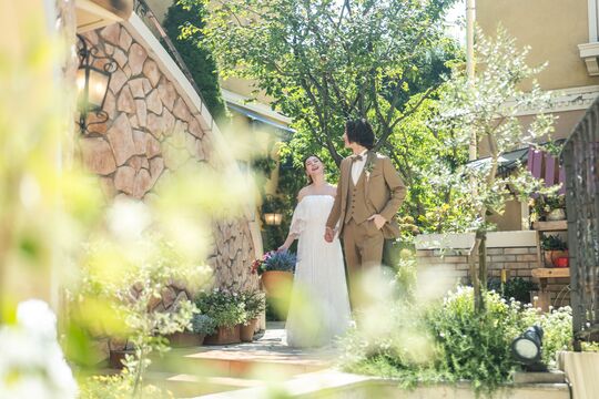 さいたま市の結婚式場アネーリ大宮。緑と光溢れる南欧風ガーデンで、手を繋ぎ歩く新郎新婦。談笑する自然な笑顔を切り取った、幸せなウェディングフォト。