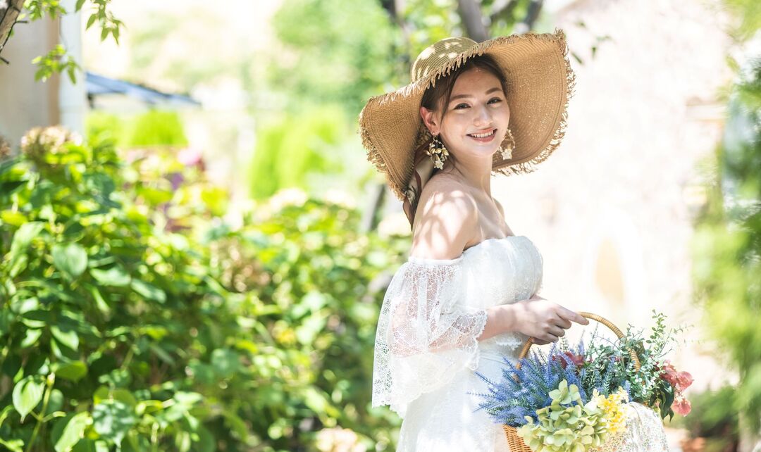 さいたま市の結婚式場アネーリ大宮。緑溢れるガーデンで、麦わら帽子を被り花かごを持つ花嫁。海外リゾートのようなナチュラルで笑顔輝く一枚。