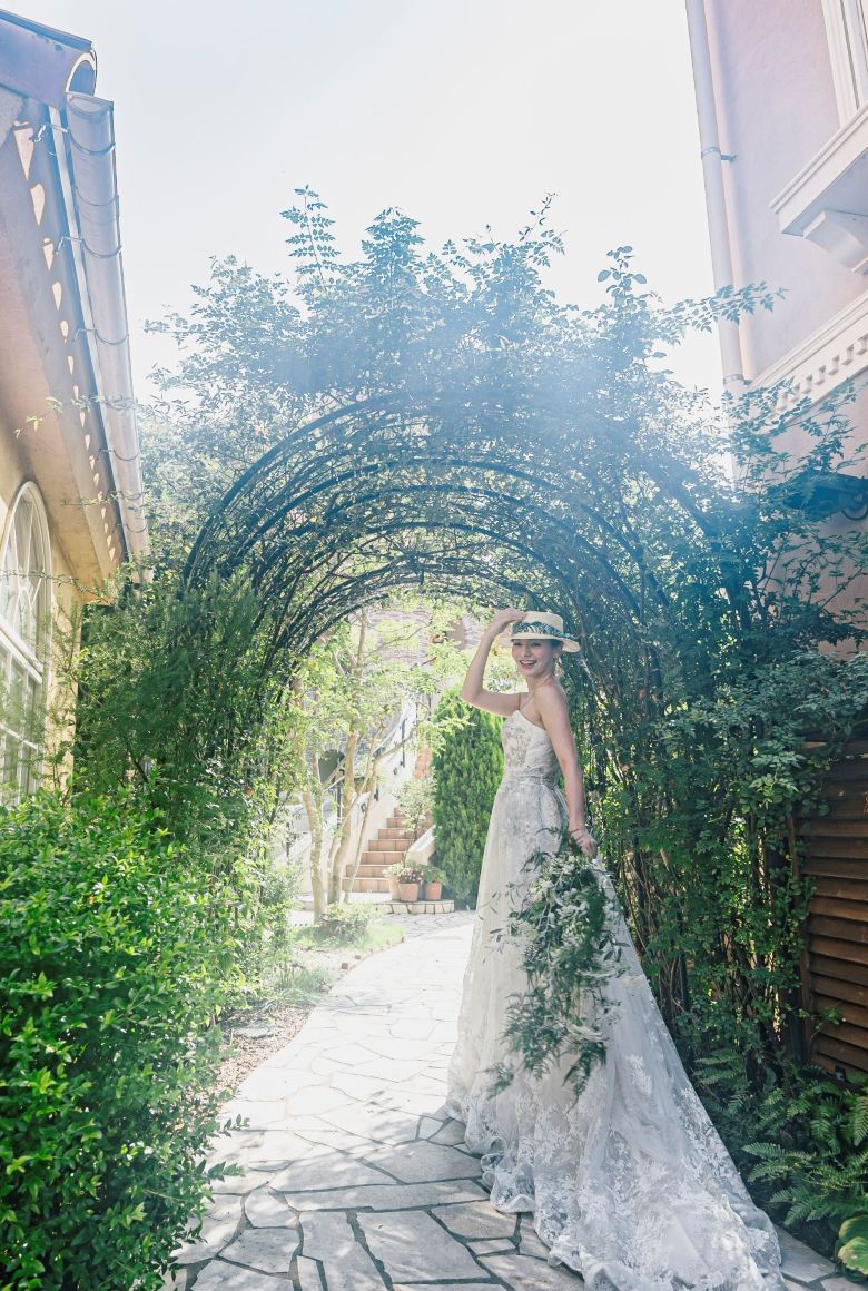 さいたま市の結婚式場アネーリ大宮。緑のアーチが続くガーデンで、木漏れ日に包まれ佇む花嫁。海外映画のようなナチュラルで幻想的なウェディングフォト。