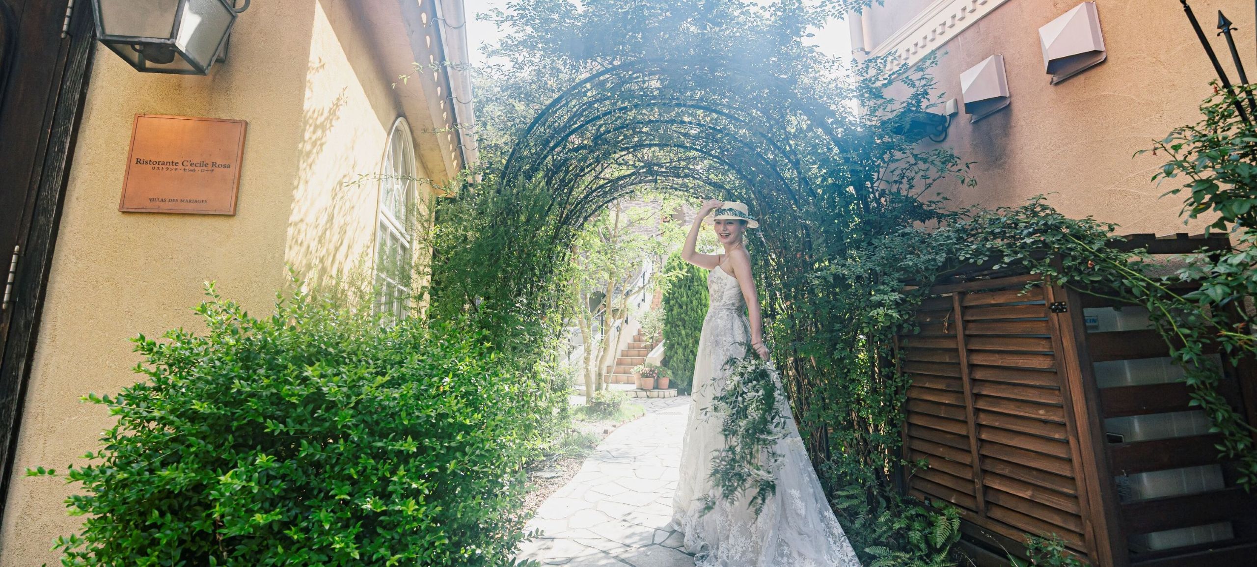 さいたま市の結婚式場アネーリ大宮。緑のアーチが続くガーデンで、木漏れ日に包まれ佇む花嫁。海外映画のようなナチュラルで幻想的なウェディングフォト。