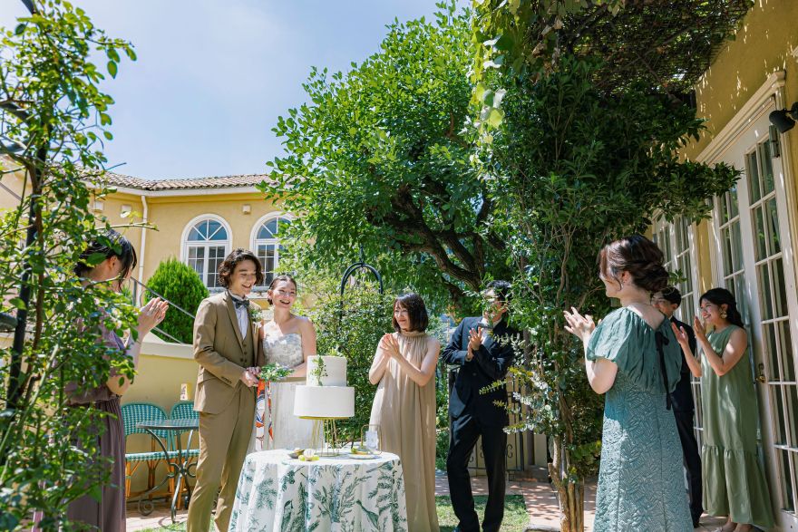 さいたま市の結婚式場アネーリ大宮。緑豊かなプライベートガーデンで、ゲストの拍手に包まれケーキ入刀。青空の下、笑顔が溢れるアットホームな結婚式。