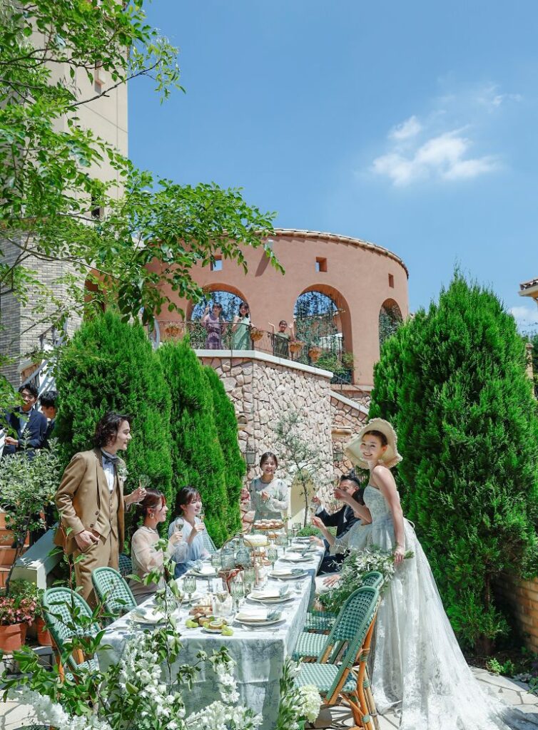 さいたま市の結婚式場アネーリ大宮。青空の下、南欧風の建物に囲まれた中庭でガーデンパーティ。ゲストの祝福と笑顔に包まれる、開放的で賑やかなウェディング。