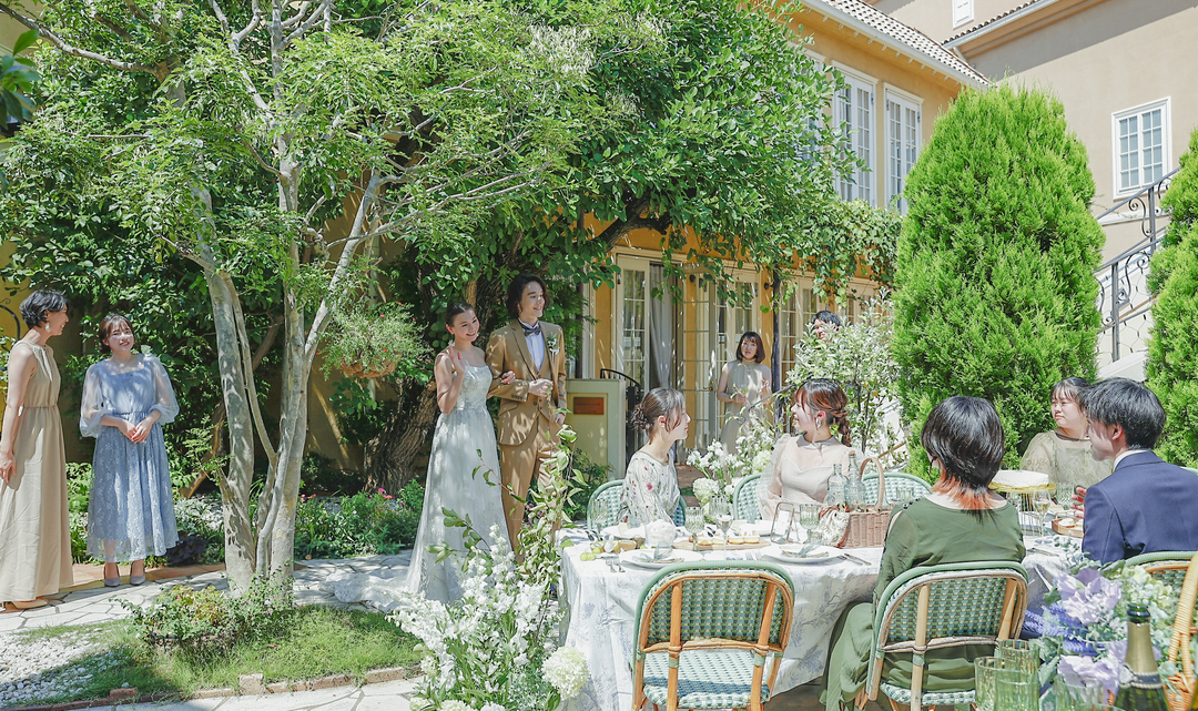 さいたま市の結婚式場アネーリ大宮。緑豊かなガーデンで、新郎新婦とゲストが笑顔で語らうアットホームなパーティ。海外邸宅のような開放的なウェディング風景。