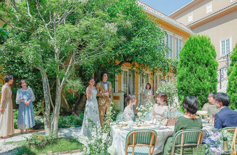 さいたま市の結婚式場アネーリ大宮。緑豊かなガーデンで、新郎新婦がゲストのテーブルを巡り、笑顔で語らう。自然体で過ごすアットホームなパーティ