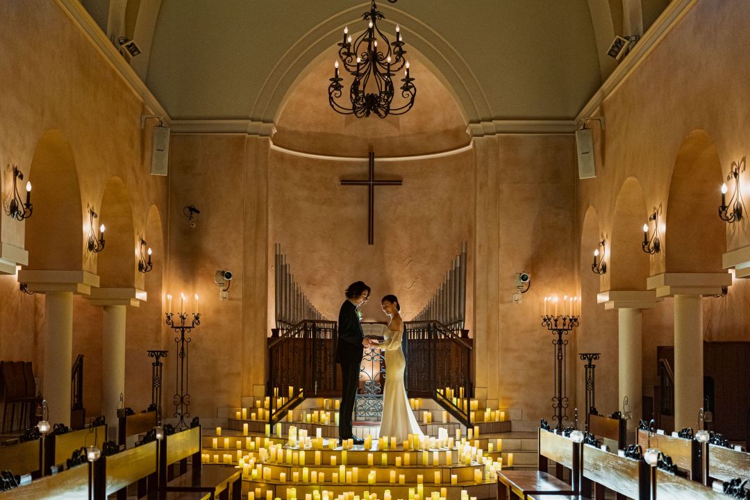 さいたま市の結婚式場アネーリ大宮。無数のキャンドルが輝く大聖堂で、手を取り合う新郎新婦。厳かでロマンティックなナイトチャペルでの挙式風景