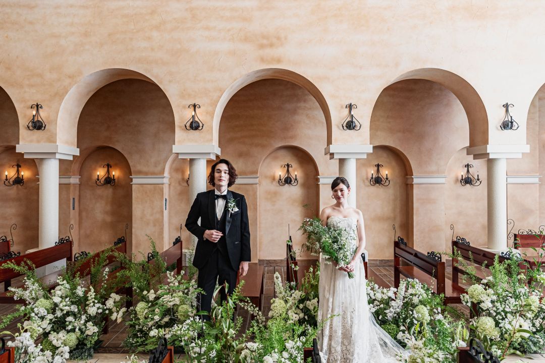 さいたま市の結婚式場アネーリ大宮。アーチが続くチャペルで、緑と花々の装飾が映える新郎新婦。クラシカルな空間で行うナチュラルウェディング