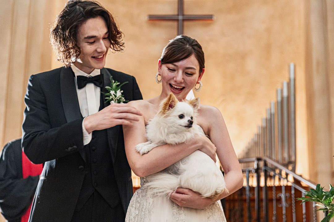 さいたま市の結婚式場アネーリ大宮。チャペルで愛犬を抱きかかえ、笑顔で祝福を受ける新郎新婦。大切な家族（ペット）と叶える感動のファミリーウェディング。