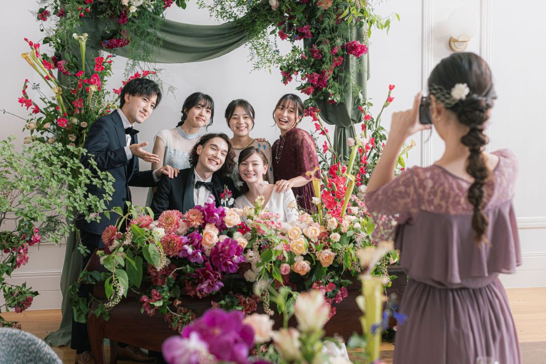 さいたま市の結婚式場アネーリ大宮。鮮やかな花々に囲まれた高砂で、新郎新婦とゲストが写真撮影。笑顔が溢れるアットホームで華やかな披露宴。