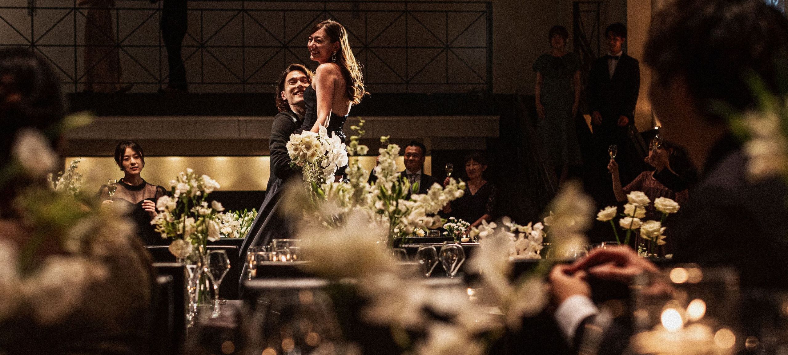 さいたま市の結婚式場アネーリ大宮。キャンドル煌めく会場で、ブラックドレスの花嫁を新郎が抱き上げる、映画のワンシーンのようなナイトウェディング。