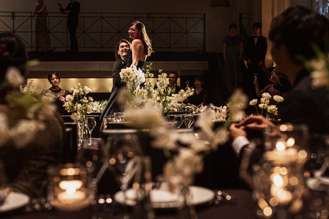 さいたま市の結婚式場アネーリ大宮。キャンドル輝くシックな会場で、新郎が花嫁を抱き上げダンス。映画のワンシーンのようなドラマチックなナイトウェディング。