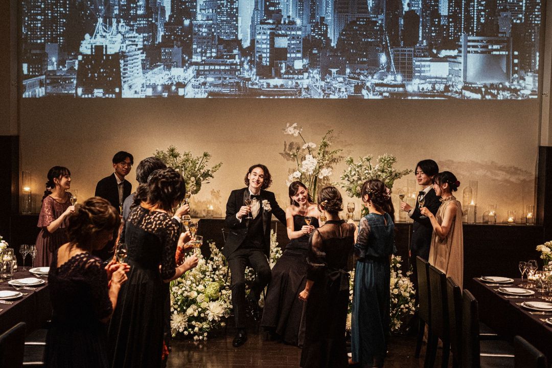 さいたま市の結婚式場アネーリ大宮。夜景の映像とキャンドルが彩る会場で、新郎新婦がゲストと乾杯。一体感が生まれる感動的なナイトウェディング。