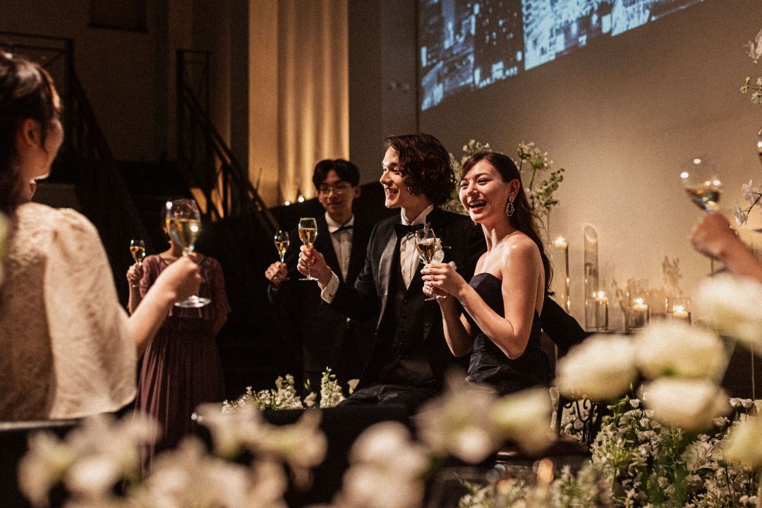 さいたま市の結婚式場アネーリ大宮。夜景の映像とキャンドルが彩る会場で、新郎新婦がゲストと乾杯。幸せな笑顔が溢れる感動的なナイトウェディング。