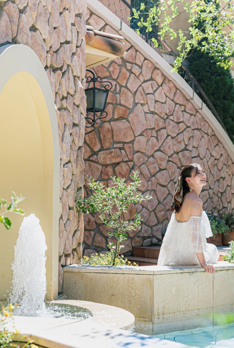 さいたま市の結婚式場アネーリ大宮。噴水が煌めく南欧風の中庭で、水辺に腰掛けリラックスする花嫁。爽やかな風と水音を感じるリゾートのような一枚。