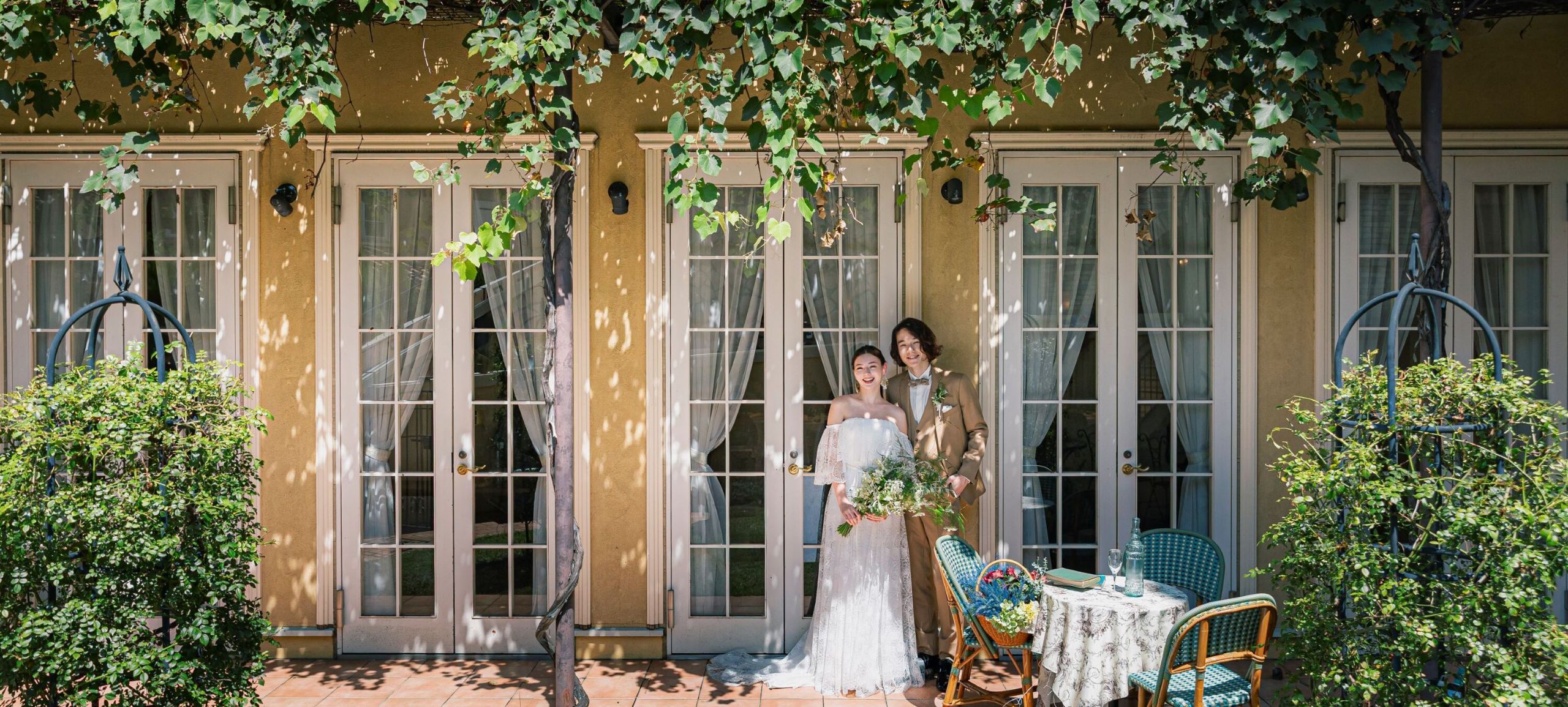 さいたま市の結婚式場アネーリ大宮。緑の蔦と木漏れ日が美しいテラスで、穏やかに微笑む新郎新婦。自然体で過ごせるナチュラルなウェディングフォト。