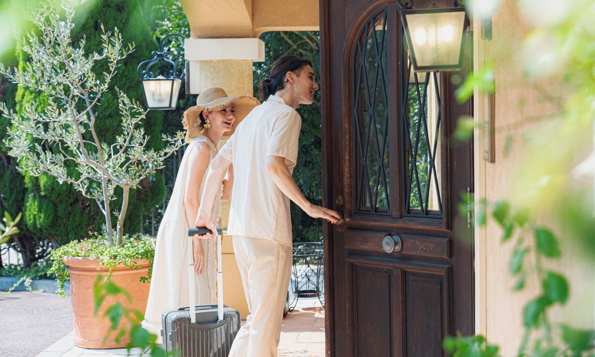 さいたま市の結婚式場アネーリ大宮。キャリーケースを手に、南欧風邸宅の扉を開けるカップル。記念日の再訪や、海外リゾート気分の非日常体験