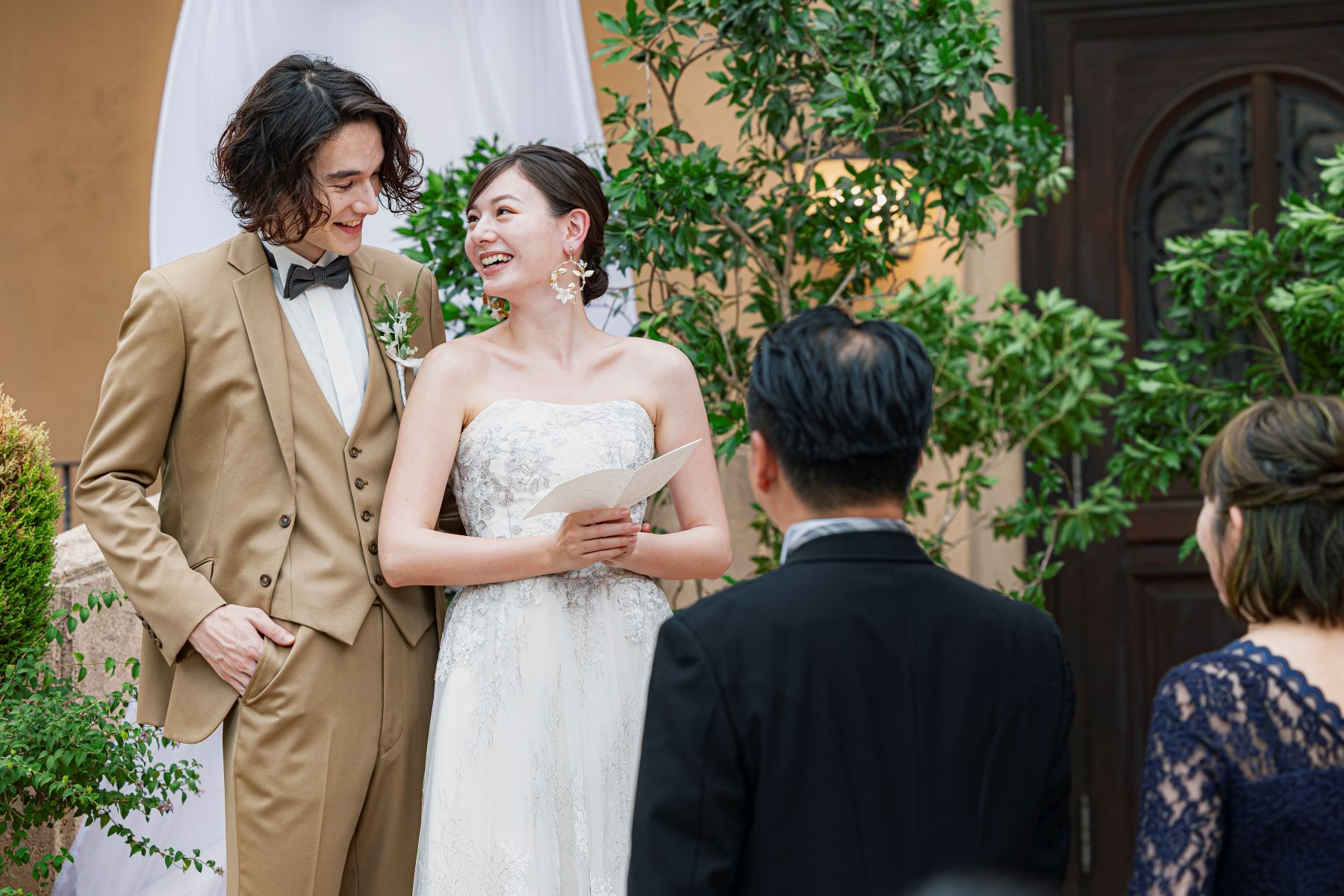 「大宮の結婚式場『アネーリ大宮』のガーデン人前式にて、手紙や誓いの言葉を交わし、笑顔で見つめ合う新郎新婦。大切なゲストに見守られながら進む、緑豊かな屋外チャペルでの開放的でアットホームな挙式シーン。」