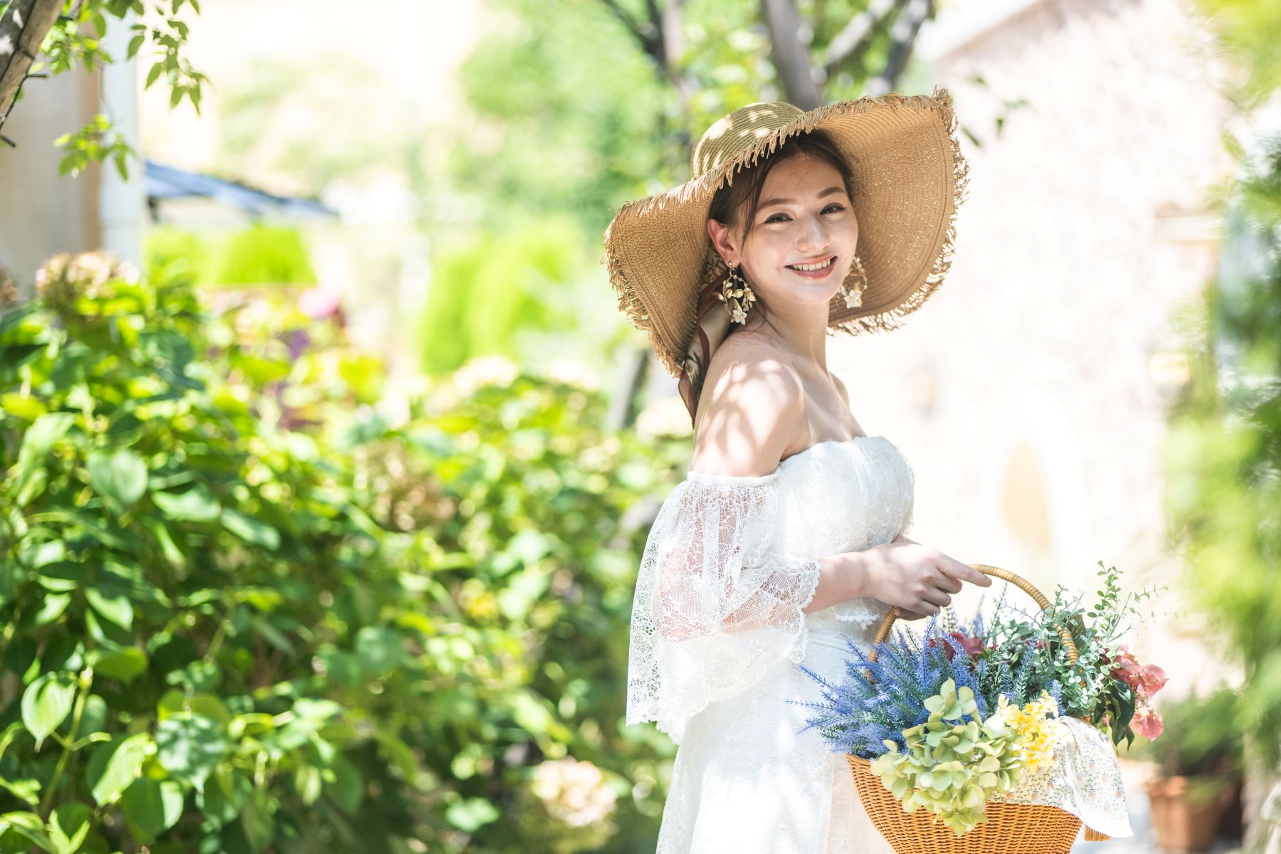 アネーリ大宮の緑豊かなガーデンで、麦わら帽子とフラワーバスケットを合わせた笑顔の花嫁。さいたま市で叶う、リゾート感あふれるナチュラルなガーデンウェディングのロケーションフォト。