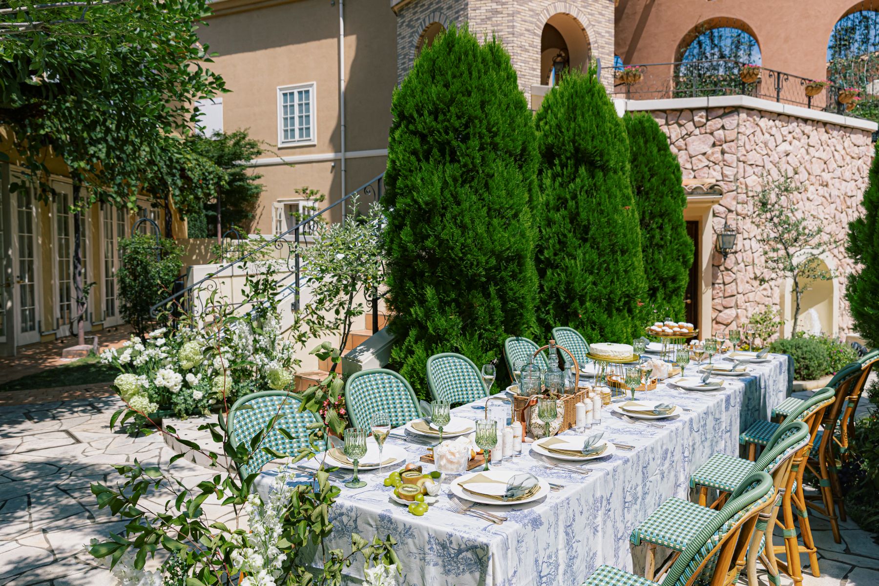 さいたま市の結婚式場「アネーリ大宮」のプライベートガーデン。南欧風の邸宅と豊かな緑に囲まれた屋外テラスに、青と白のテーブルクロスやグリーンのグラスで彩られた上質なパーティーコーディネートが並ぶ、開放感あふれるガーデンウェディングの風景。