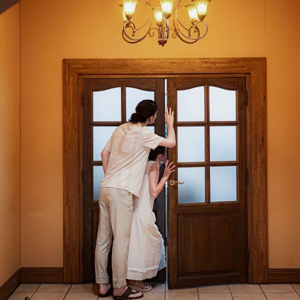 さいたま市の結婚式場「アネーリ大宮」で行われる結婚3周年記念式「ノス・ド・フロマン」。アンティークな木製の扉をそっと開き、これから始まるセレモニーに期待を寄せて中を覗き込むカジュアルな装いの夫婦。温かなシャンデリアの光に包まれた、挙式後も続く特別な絆を感じさせるアニバーサリーのワンシーン。