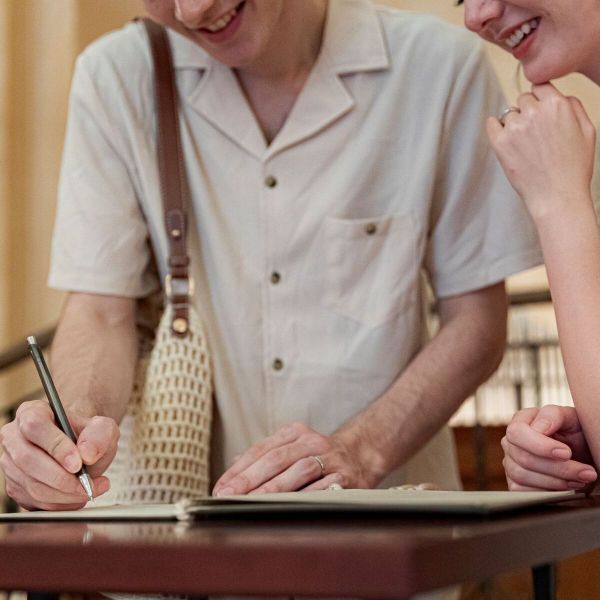 さいたま市の結婚式場「アネーリ大宮」で行われる結婚3周年記念式「ノス・ド・フロマン」。特別なアニバーサリーの思い出を刻むように、笑顔で記念の署名を行う夫婦の手元と幸せあふれる表情のアップ。挙式後も続く家族の絆を形に残す、心温まるセレモニーのワンシーン。