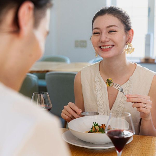 さいたま市の結婚式場「アネーリ大宮」で行われる結婚3周年記念式「ノス・ド・フロマン」のアニバーサリーランチ。白を基調とした明るい空間で、彩り豊かな特別コース料理と赤ワインを楽しみながら、幸せそうな笑顔を浮かべる女性。挙式後も思い出の場所で大切な節目を祝う、特別な食体験をイメージした一枚。