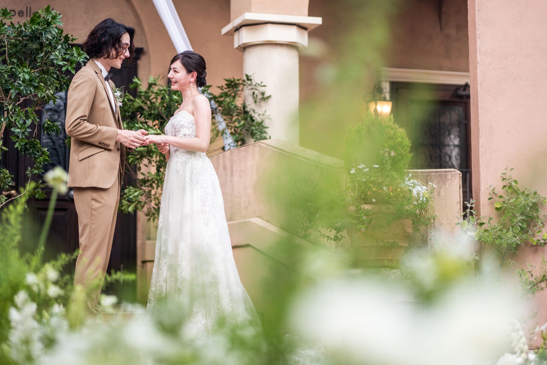 「大宮の結婚式場『アネーリ大宮』の緑豊かなガーデン人前式での指輪交換のシーン。ナチュラルな屋外チャペルを舞台に、見つめ合う新郎新婦の温かな誓いの瞬間を捉えた、アットホームで開放感あふれるウェディングフォト。」