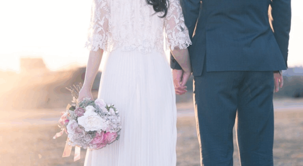 【さいたま市結婚式場アネーリ大宮】の広大なロケーションにて、夕暮れ時の光を浴びながら手を繋ぐウェディングドレス姿の新婦様と新郎様。さいたま市にある市の式場で叶える、ドラマチックな前撮りを詳細に描写しており、さいたま市内での結婚式らしい、情緒溢れる美しい一瞬を表現しています。