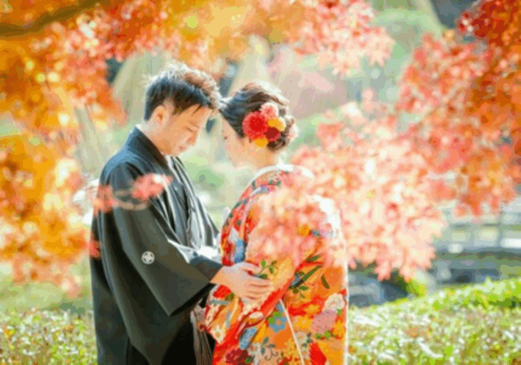 【さいたま市結婚式場アネーリ大宮】の庭園にて、鮮やかな紅葉に包まれながら寄り添う紋付袴姿の新郎様と色打掛姿の新婦様。さいたま市にある市の式場で叶える、秋の絶景ロケーションを詳細に描写しており、さいたま市内での結婚式らしい、風情ある感動の瞬間を表現しています