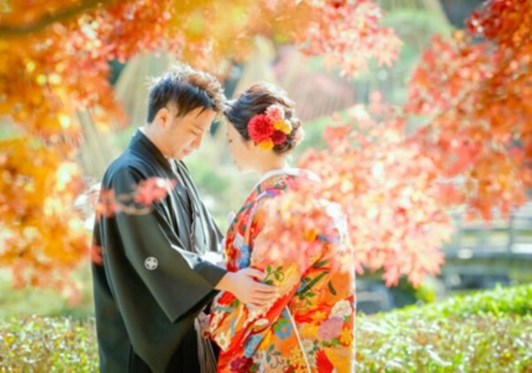 【さいたま市結婚式場アネーリ大宮】の庭園にて、鮮やかな紅葉に包まれながら寄り添う紋付袴姿の新郎様と色打掛姿の新婦様。さいたま市にある市の式場で叶える、秋の絶景ロケーションを詳細に描写しており、さいたま市内での結婚式らしい、風情ある感動の瞬間を表現しています