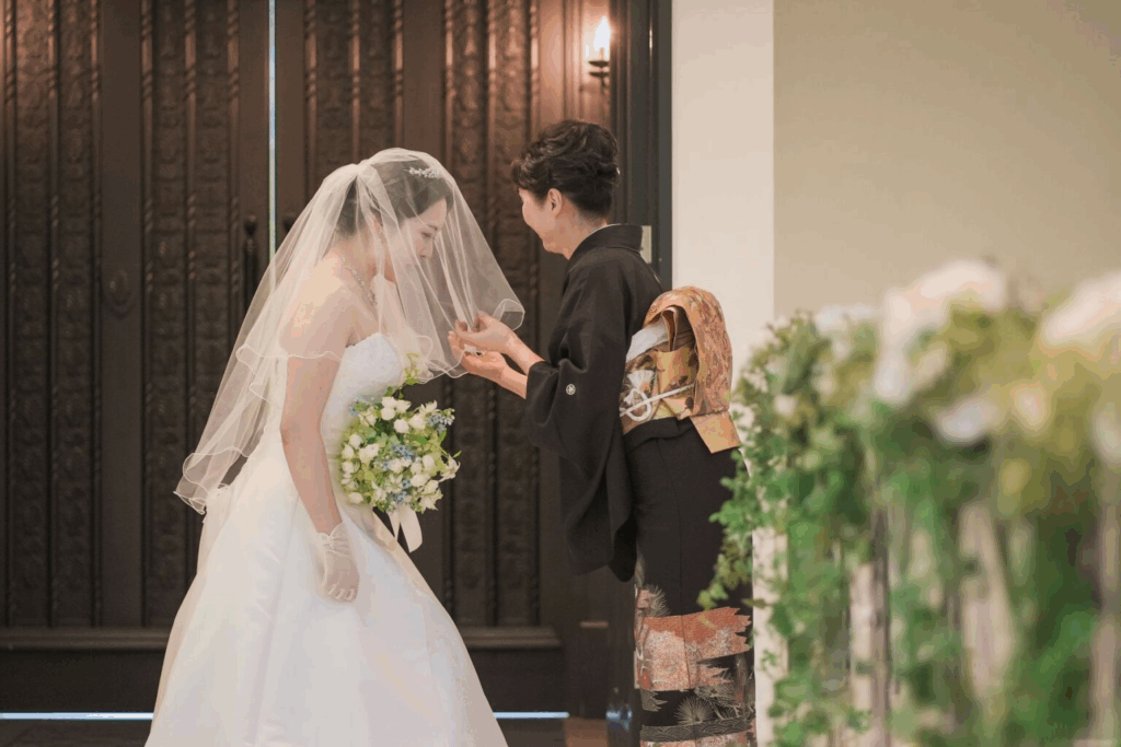 【さいたま市結婚式場アネーリ大宮】の開放的な屋外にて、長いベールに包まれながら静かに誓いのキスを交わす新郎新婦様。さいたま市にある市の式場で叶える、ベールダウンから続く神聖なセレモニーを詳細に描写しており、さいたま市内での結婚式らしい、深い愛と感動に満ちたウェディングシーンを表現しています。