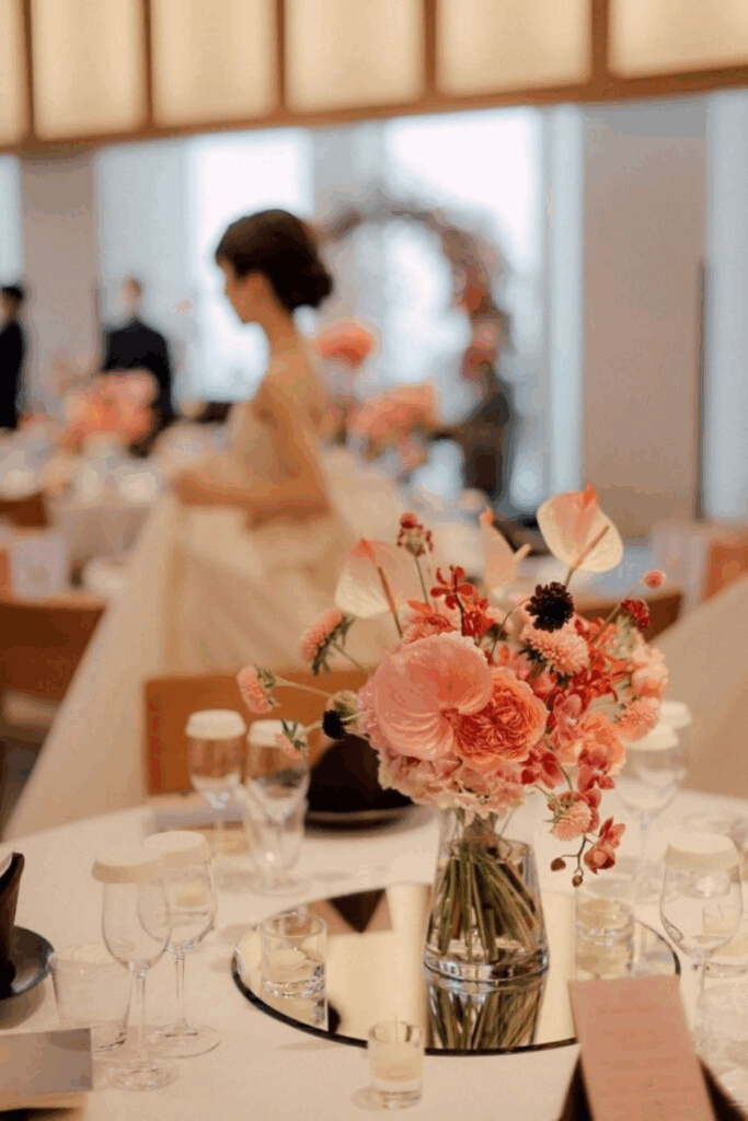 【さいたま市結婚式場アネーリ大宮】の披露宴会場にて、ミラーの上に飾られたモダンな暖色系のテーブル装花。さいたま市にある市の式場で叶える、上質な空間演出を詳細に描写しており、さいたま市内での結婚式らしい、華やかでセンス溢れるパーティーの情景を表現しています。