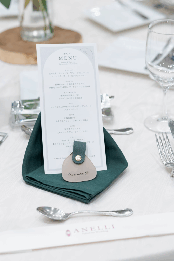 【さいたま市結婚式場アネーリ大宮】の披露宴会場にて、上質なナプキンの上に美しく配置された婚礼料理のメニュー表。さいたま市にある市の式場で提供される、地元の旬の食材を活かした絶品コースを詳細に描写しており、さいたま市内での結婚式らしい、五感で楽しむ贅沢なおもてなしを表現しています。