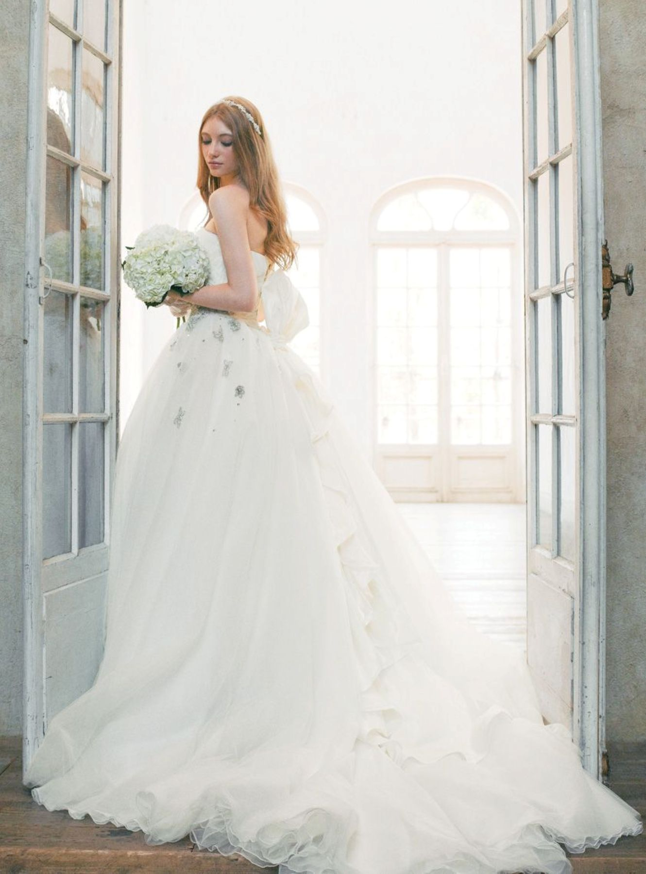 【さいたま市結婚式場アネーリ大宮】の光り輝く扉の前で、白く瑞々しいブーケを手に佇む花嫁様。さいたま市にある市の式場で叶える、洗練されたインポートドレスの美しさを詳細に描写しており、さいたま市内での結婚式を象徴するような上品で清らかな世界観を表現しています。