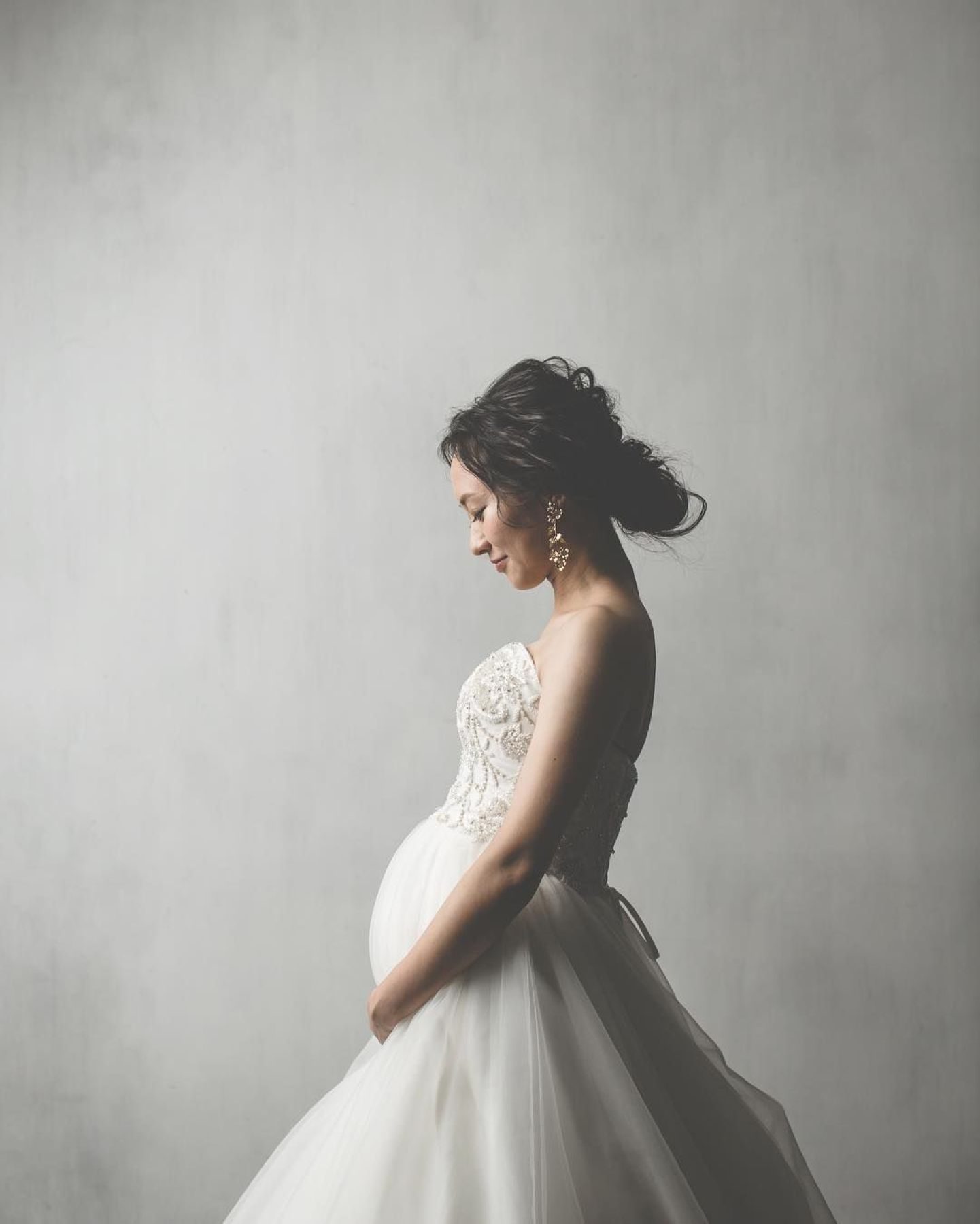 【さいたま市結婚式場アネーリ大宮】の柔らかな光の中で、お腹を優しく愛おしむマタニティ姿の花嫁様。さいたま市にある市の式場で叶える、神秘的で美しい瞬間を詳細に描写しており、さいたま市内での結婚式がお二人と赤ちゃんにとって最高の門出となるよう願いを込めています。