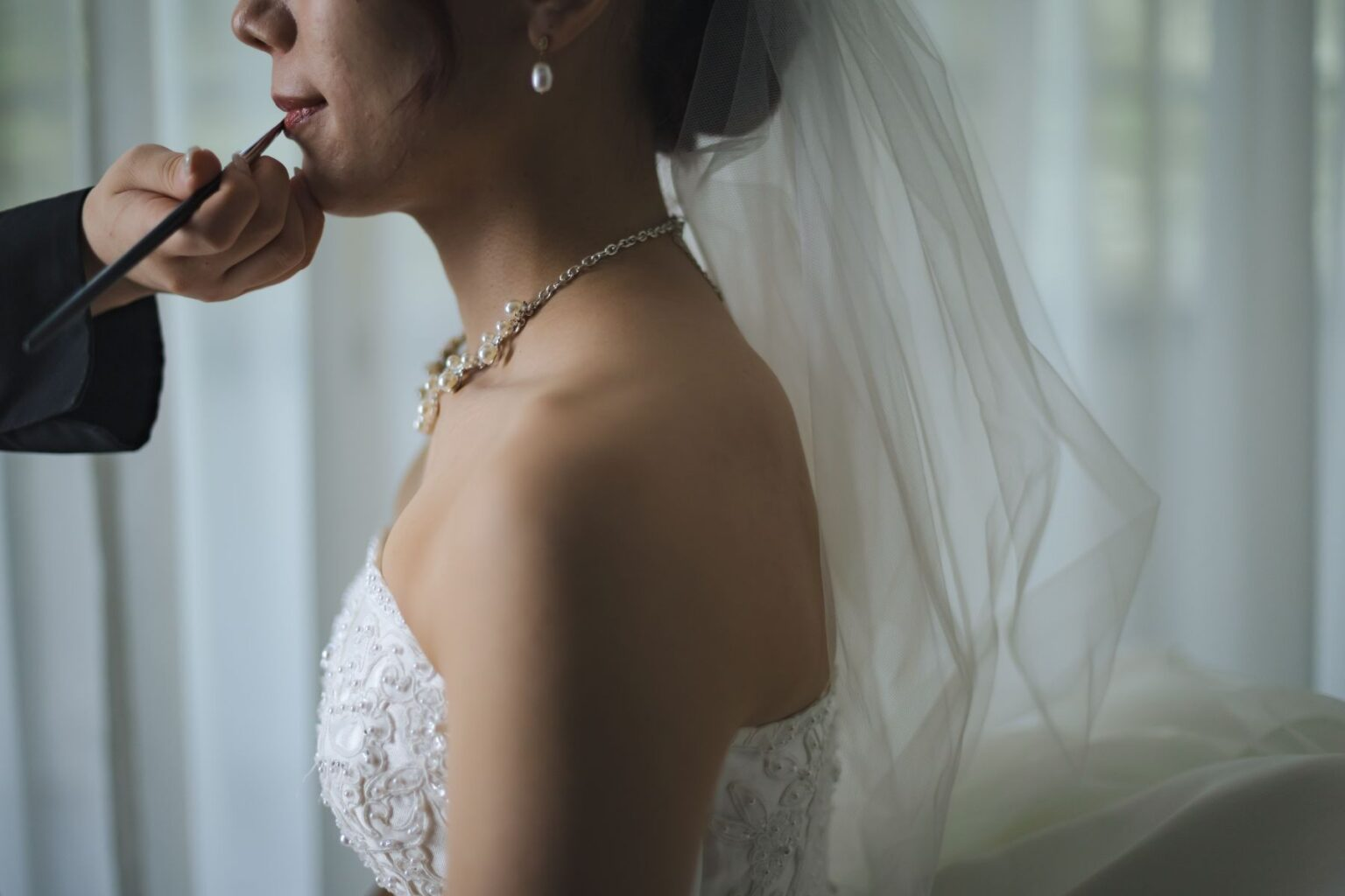 【さいたま市結婚式場アネーリ大宮】のブライズルームにて、プロの手で美しくメイクアップを仕上げる花嫁様。さいたま市にある市の中心部で叶える、特別な一日が始まる高揚感を詳細に描写しており、さいたま市内での結婚式を控えた花嫁様の純粋な美しさを引き立てています。