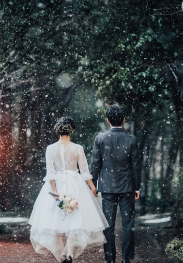 【さいたま市結婚式場アネーリ大宮】の豊かな緑が雪に彩られた中、手をつなぎ未来へ歩む新郎新婦様のバックスタイル。さいたま市にある市の式場で叶える、冬ならではのロマンチックな光景を詳細に描写しており、さいたま市内での結婚式をよりドラマチックに演出する特別な瞬間を表現しています。