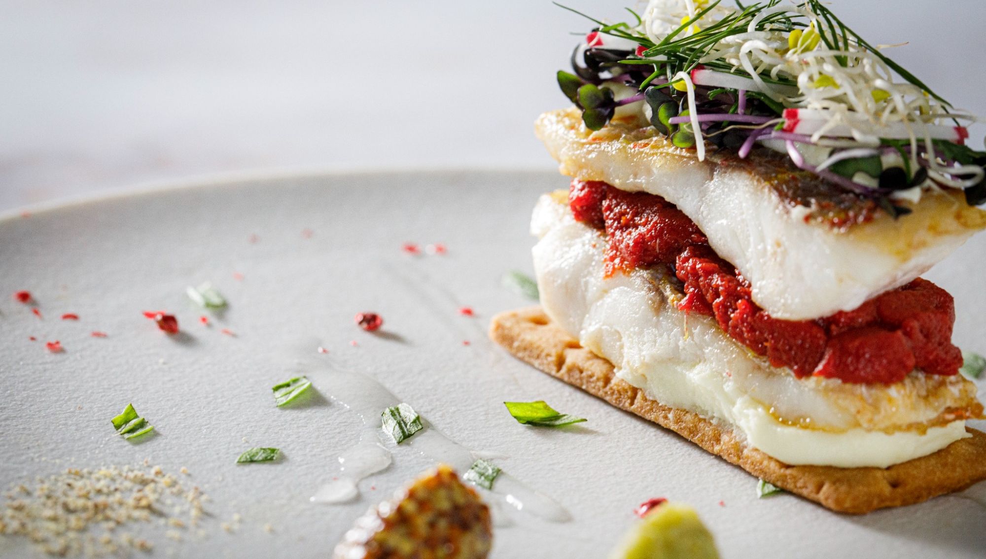 アネーリ大宮の婚礼料理。サクサクの生地に白身魚のポワレと赤いソースを重ねたミルフィーユ仕立ての一皿。マイクログリーンを添えた、大宮の結婚式場でゲストを魅了する本格フレンチの魚料理。