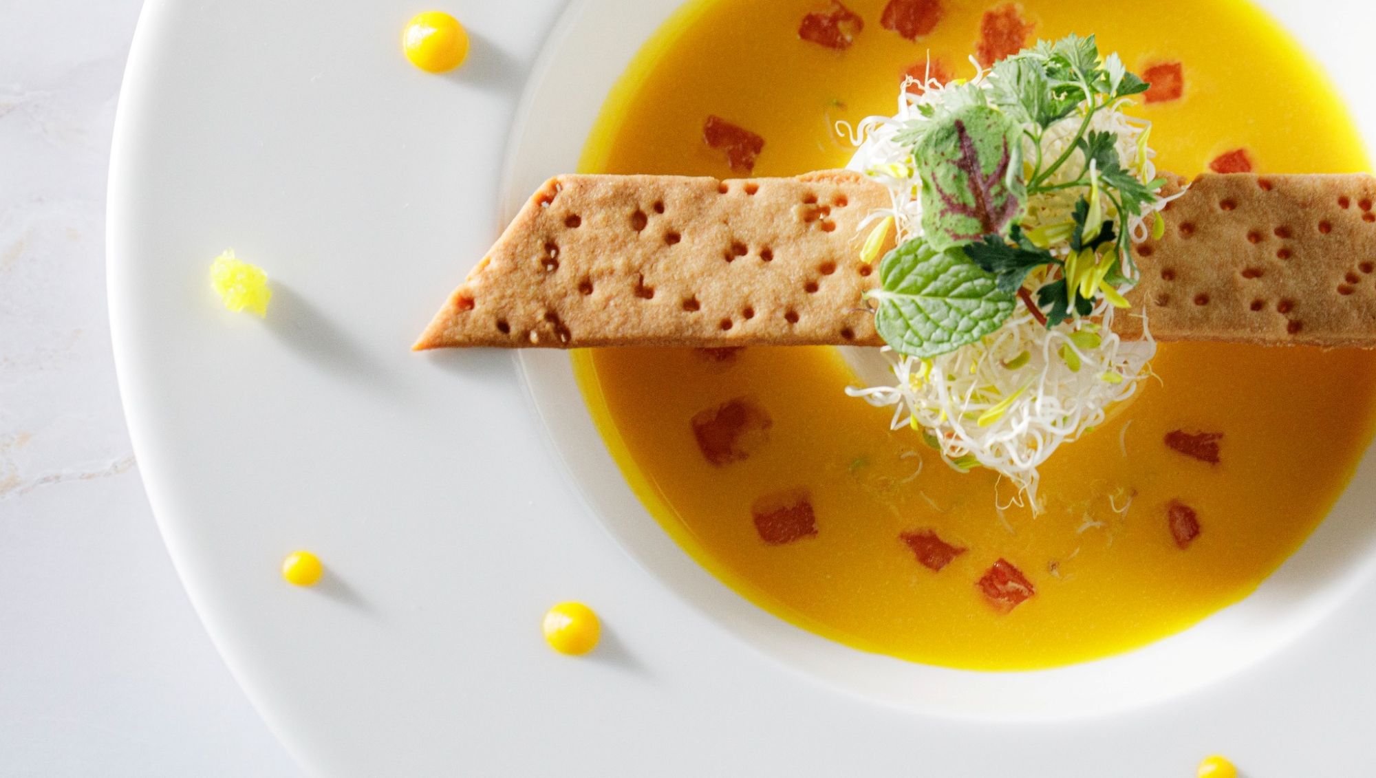 アネーリ大宮の婚礼料理。鮮やかなイエローのポタージュスープに、香ばしいクリスプと彩り豊かなハーブを添えた一皿。大宮の結婚式場で提供される、五感で楽しむ本格フレンチコースのスープ料理。