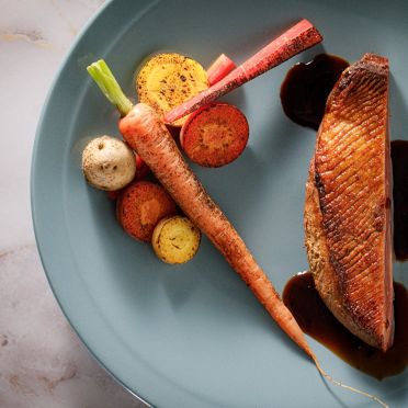 アネーリ大宮の婚礼料理。美しい焼き目がついた鴨胸肉のローストに、丸ごとの人参と彩り豊かな根菜を添えて。大宮の結婚式場でゲストに振る舞われる、素材の旨みを凝縮した本格フレンチの鴨料理。