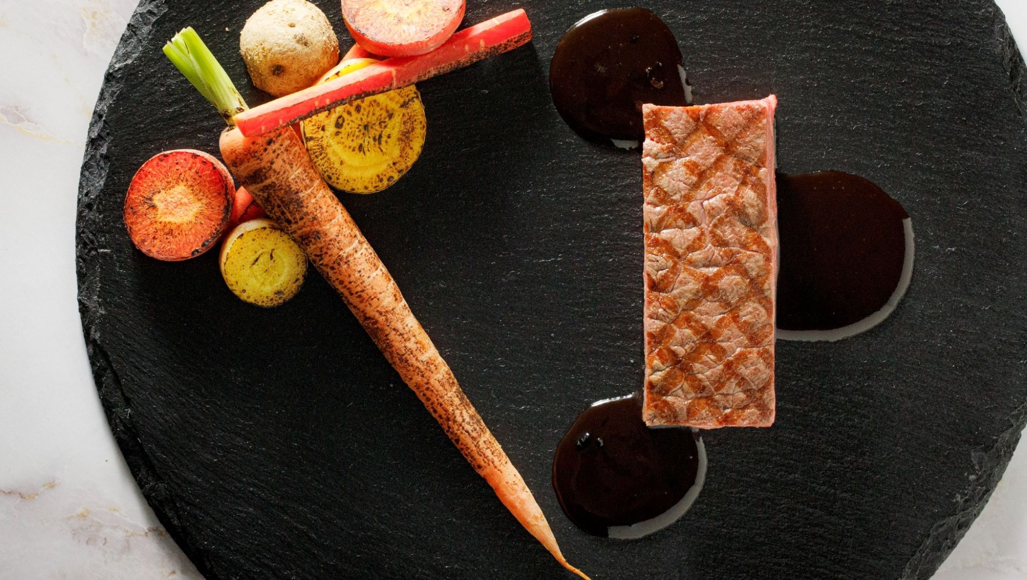 アネーリ大宮の婚礼料理。黒のスレート皿に美しく盛り付けられた牛フィレ肉のグリルと一本のローストキャロット、赤ワインソース。大宮の結婚式場で提供される本格フレンチの一皿。