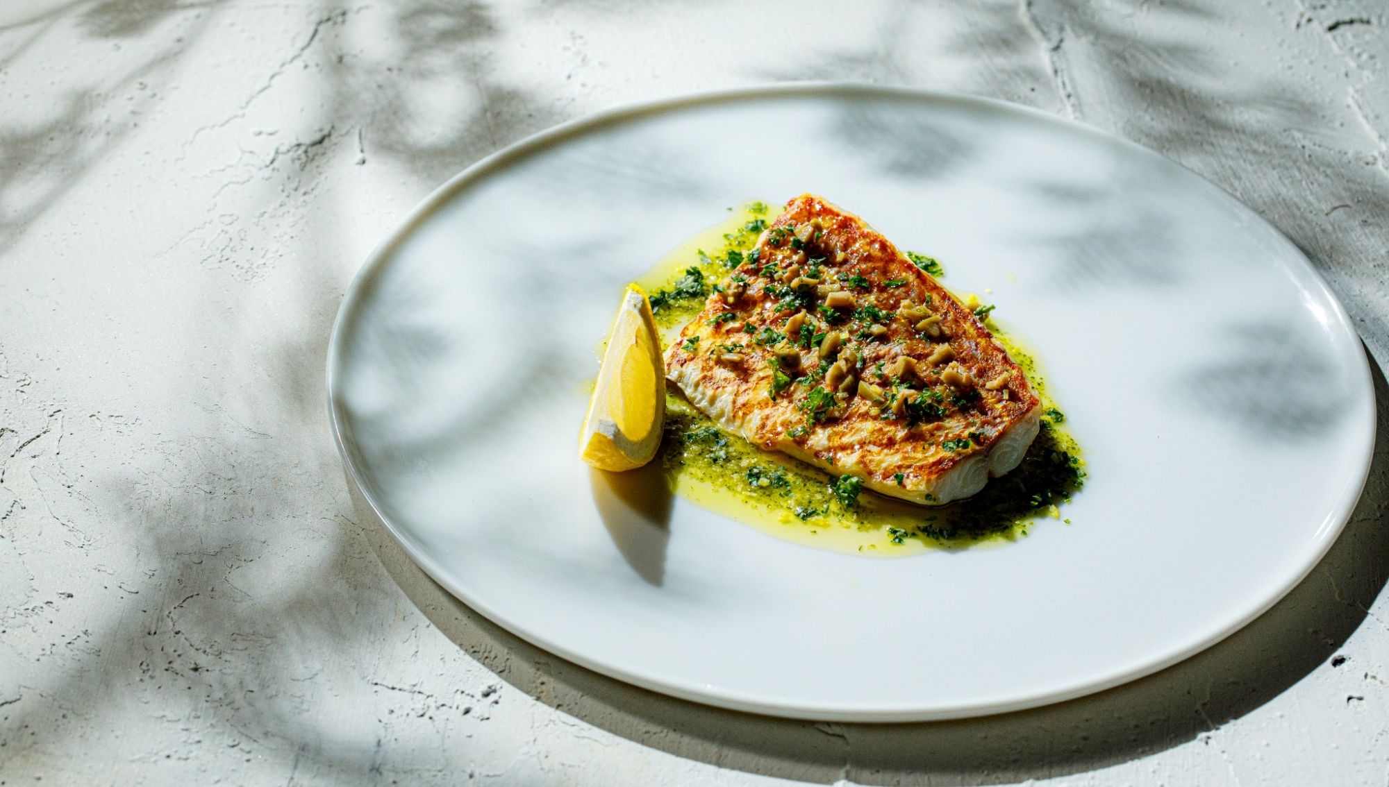 アネーリ大宮の婚礼料理。木漏れ日のような光が差し込む白い皿に、鮮やかな香草ソースとレモンを添えた白身魚のポワレ。大宮の結婚式場でゲストに提供される、素材の鮮度が際立つ本格フレンチの魚料理