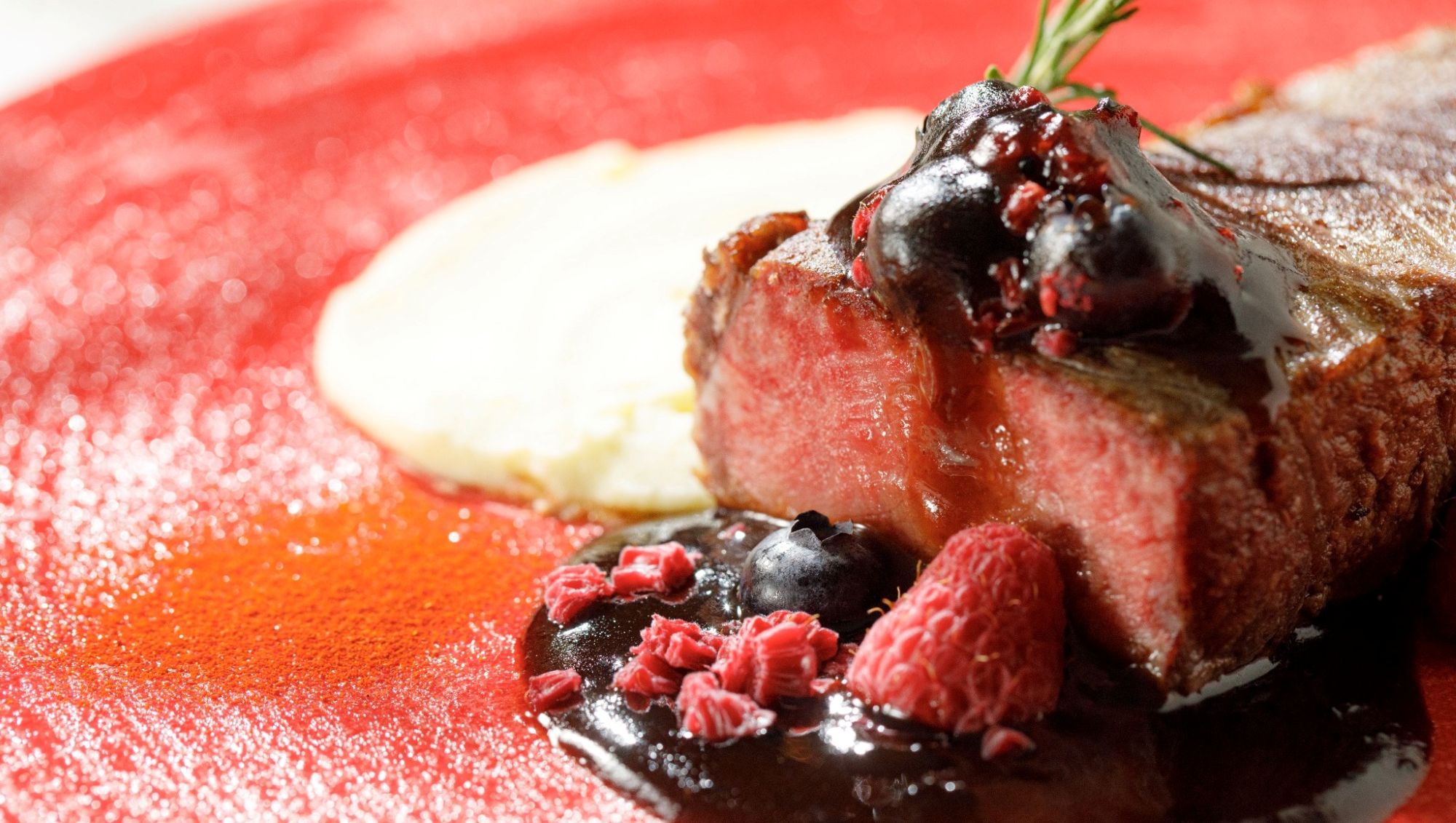 アネーリ大宮の婚礼料理。ブルーベリーやラズベリーのソースを添えた牛フィレ肉のステーキ。鮮やかな赤のプレートに盛り付けられた、華やかでモダンな結婚式のメインディッシュ。